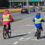 2 dzieci w kamizelkach jadą na rowerach ścieżką rowerową