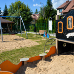 Plac zabaw: piaskownica, huśtawki, w tle altana.