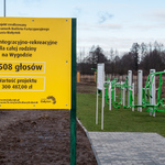 Żółta tabliczka ustawiona na terenie siłowni, informująca, iż inwestycja została zrealizowana w ramach Budżetu Partycypacyjnego 2015
