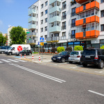 Samochody stoją na parkingu usytuowanym między jezdną a blokiem mieszkalnym
