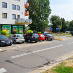 Samochody stoją na parkingu usytuowanym między jezdną a blokiem mieszkalnym