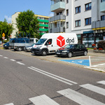 Samochody stoją na parkingu usytuowanym między jezdną a blokiem mieszkalnym