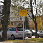 Samochody zaparkowane na parkingu oznakowanym żółtą tabliczką informującą o realizacji inwestycji w ramach budżetu obywatelskiego