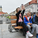 Dziewczyna i dwóch chłopców siedzą na ławce solarnej i korzystają z telefonów komórkowych.