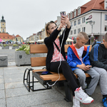 Dziewczyna i dwóch chłopców siedzą na ławce solarnej i korzystają z telefonów komórkowych.