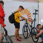 W centrum mężczyzna stojący przy rowerze i przytrzymujący go. Drugi mężczyzna pochyla się przy rowerze.