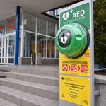 Na pierwszym planie defibrylator AED, w tle schody i budynek urzędu miejskiego.