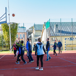 Zewnętrzne boisko szkolne z poliuretanu. Kilka młodych osób gra w koszykówkę.