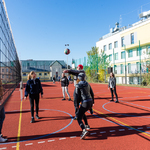 Zewnętrzne boisko szkolne z poliuretanu. Kilka młodych osób gra w siatkówkę.