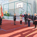Zdjęcie z otwarcia boiska. Prezydent Białegostoku i kilka innych osób stoi na płycie boiska. Prezydent przecina wstęgę.