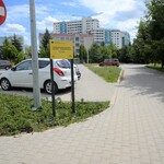 Parking wraz z drogą manewrową. Na parkingu samochody. Tabliczka żółta zawierająca informację o realizacji projektu z Budżetu Obywatelskiego.