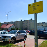 Parking, kilka samochodów. Żółta tablica informacyjna na słupie. w oddali bloki.