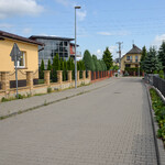 Widok na ulicę z kostki brukowej. Ogrodzenia budynków mieszkalnych. w tle drzewa i budynki.