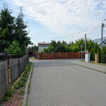 Widok na ulicę z kostki brukowej. Ogrodzenia budynków mieszkalnych. w tle drzewa i budynki.