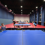 Wnętrze sali gimnastycznej. Na pierwszym planie widok na podłogę, dalej młodzi lidzie grają przy stołach w pingponga.