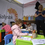 Widok na wnętrze namiotu. Dzieci kolorują książeczki przy kolorowych stolikach.  Kobieta stoi.