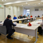 Przestronne jasne pomieszczenie. Kilkanaście osób siedzi przy stołach ostawionych w duży okrąg.