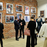 Uczestnicy wernisażu skupieni w małych grupkach. Kilka osób robi telefonami zdjęcia fotografiom wiszącym na ścianach.