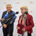 Prezydent Miasta oraz kobieta w czerwonej bluzce stoją przed kilkoma mikrofonami na statywach. Kobieta mówi do jednego z nich.