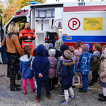 Ratownik medyczny szkoli dzieci z udzielania pierwszej pomocy. W tle ambulans.