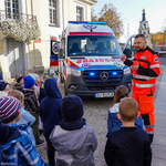 Ratownik medyczny szkoli dzieci z udzielania pierwszej pomocy. W tle ambulans przed pałacykiem gościnnym przy ulicy Kilińskiego.
