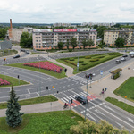 Przestrzeń miejska widziana z góry. Kilka krzyżujących się ze sobą ulic przedzielonych pasami zieleni. Przy jednej z ulic przystanek autobusowy porośnięty zielenią. 