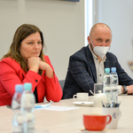 Kobieta w czerwonej marynarce oraz mężczyzna w marynarce w kratkę siedzą przy stole.