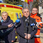 Dyrektor Stacji Pogotowia Ratunkowego mówi do mikrofonów skierowanych w jego stronę. Obok stoi Prezydent Białegostoku i mężczyzna w jaskrawej kurtce. 