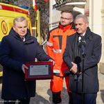 Prezydent Białegostoku trzyma w dłoniach tabliczkę pamiątkową. Obok stoi Dyrektor Pogotowia i mężczyzna w jaskrawej kurtce.   