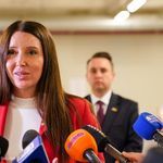 Kobieta w czerwonej marynarce mówi do mikrofonów. Za nią widoczny zastępca prezydenta.