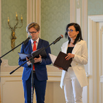 Wnętrze auli. Kobieta i mężczyzna prowadzący spotkanie stoją mówią do zgromadzonych.