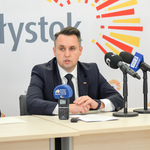 Zastępca prezydenta mówi do mikrofonów ustawionych na stole. 