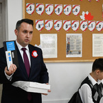 Korytarz szkolny. Zastępca prezydenta prezentuje dziennikarzom jeden z tabletów przekazanych dzieciom. 