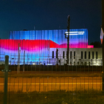 Bryła Muzeum Pamięci Sybiru nocą. Na Elewacji wyświetlone biało czerwone barwy oraz logo Muzeum Pamięci Sybiru.