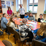 Sala szkolna. Grupka dzieci siedzi przy dużym stole ustawionym na środku sali.