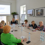 Uczestnicy spotkania siedzą przy dużym stole. W tle na ekranie projekcyjnym wyświetla się napis Program polityki senioralnej Miasta Białegostoku na lata 2023- 2025