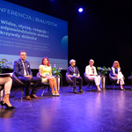 Scena Kina Forum. Siedem osób biorących udział w panelu dyskusyjnym siedzi na fotelach. Za nimi, na kinowym ekranie, wyświetlona jest plansza z tytułem konferencji.