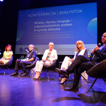 Scena Kina Forum. Siedem osób biorących udział w panelu dyskusyjnym siedzi na fotelach. Za nimi, na kinowym ekranie, wyświetlona jest plansza z tytułem konferencji. 