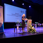 Scena Kina Forum. Prelegentka mówi do zebranych stojąc przy mównicy. W tle, na ekranie, wyświetlona jest plansza prezentacji.