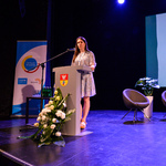 Scena Kina Forum. Prelegentka mówi do zebranych stojąc przy mównicy. W tle, na ekranie, wyświetlona jest plansza prezentacji dotycząca telefonu zaufania.