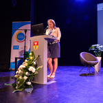 Scena Kina Forum. Prelegentka mówi do zebranych stojąc przy mównicy. W tle, na ekranie, wyświetlona jest plansza prezentacji dotycząca mieszkań interwencyjnych.