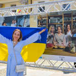 Młoda kobieta trzymająca w dłoniach flagę Ukrainy pozuje do zdjęcia  obok planszy z wystawy.