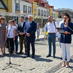 Otwarcie wystawy. Prowadząca wydarzenie dyrektorka Centrum aktywności Społecznej mówi do mikrofonu. Obok niej stoi uczestnik projektu Wspólnie, autor zdjęć, prezydent miasta i jego zastępca oraz przedstawiciele delegacji z Łucka. W tle stoi wystawa. 