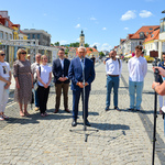 Otwarcie wystawy. Prowadząca wydarzenie dyrektorka Centrum aktywności Społecznej mówi do mikrofonu. Obok niej stoi uczestnik projektu Wspólnie, autor zdjęć, prezydent miasta i jego zastępca oraz przedstawiciele delegacji z Łucka. W tle stoi wystawa. 