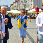 W centrum zdjęcia młoda kobieta okrywająca ramiona flagą Ukrainy. Na pierwszym planie rozmyte postacie uczestników otwarcia wystawy. 