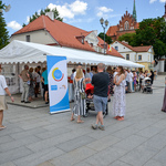 Namiot pod którym odbywają się warsztaty z pieczenia chleba. Pod i przy namiocie stoi dużo osób. Przy namiocie stoi rollup z logo Centrum Splino, Unicefu i Miasta Białystok.  