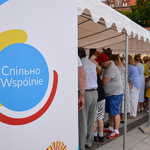 Namiot pod którym odbywają się warsztaty z pieczenia chleba. Pod i przy namiocie stoi dużo osób. Przy namiocie stoi rollup. Widać fragment z logo Centrum Splino.
