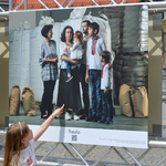 Długowłosa dziewczynka stoi przy jednej z planszy wystawowych. Wskazuje palcem kobietę na zdjęciu.  