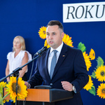 Zastępca prezydenta mówi do zebranych na sali dzieci i rodziców stojąc przy mównicy.