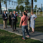 Przestrzeń siłowni pod chmurką przy ul. Szkolnej. Przedstawiciele Urzędu Miejskiego stoją na jednej z alejek w otoczeniu dziennikarzy.